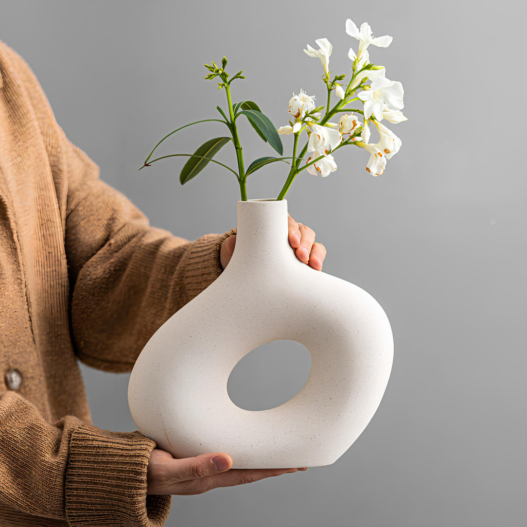 Person holding a white ceramic vase with flowers against a gray background