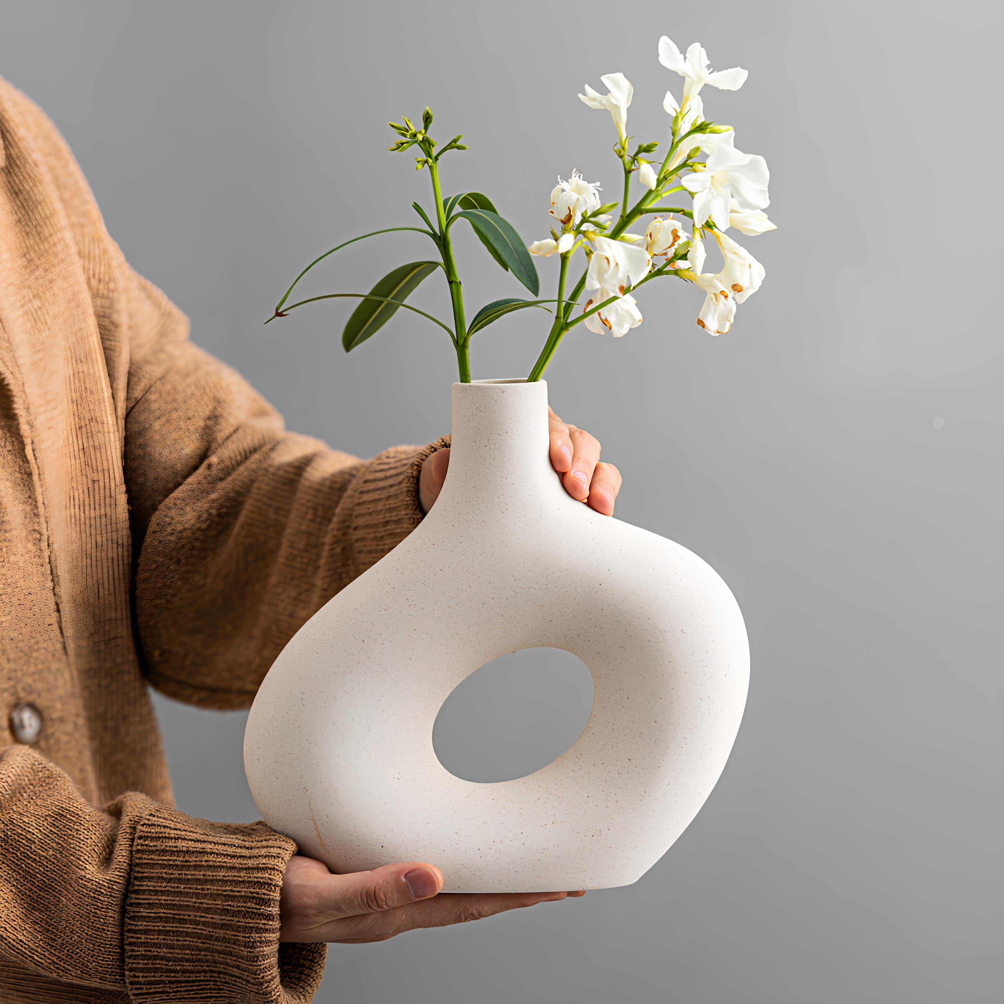 Person holding a white ceramic vase with flowers against a gray background