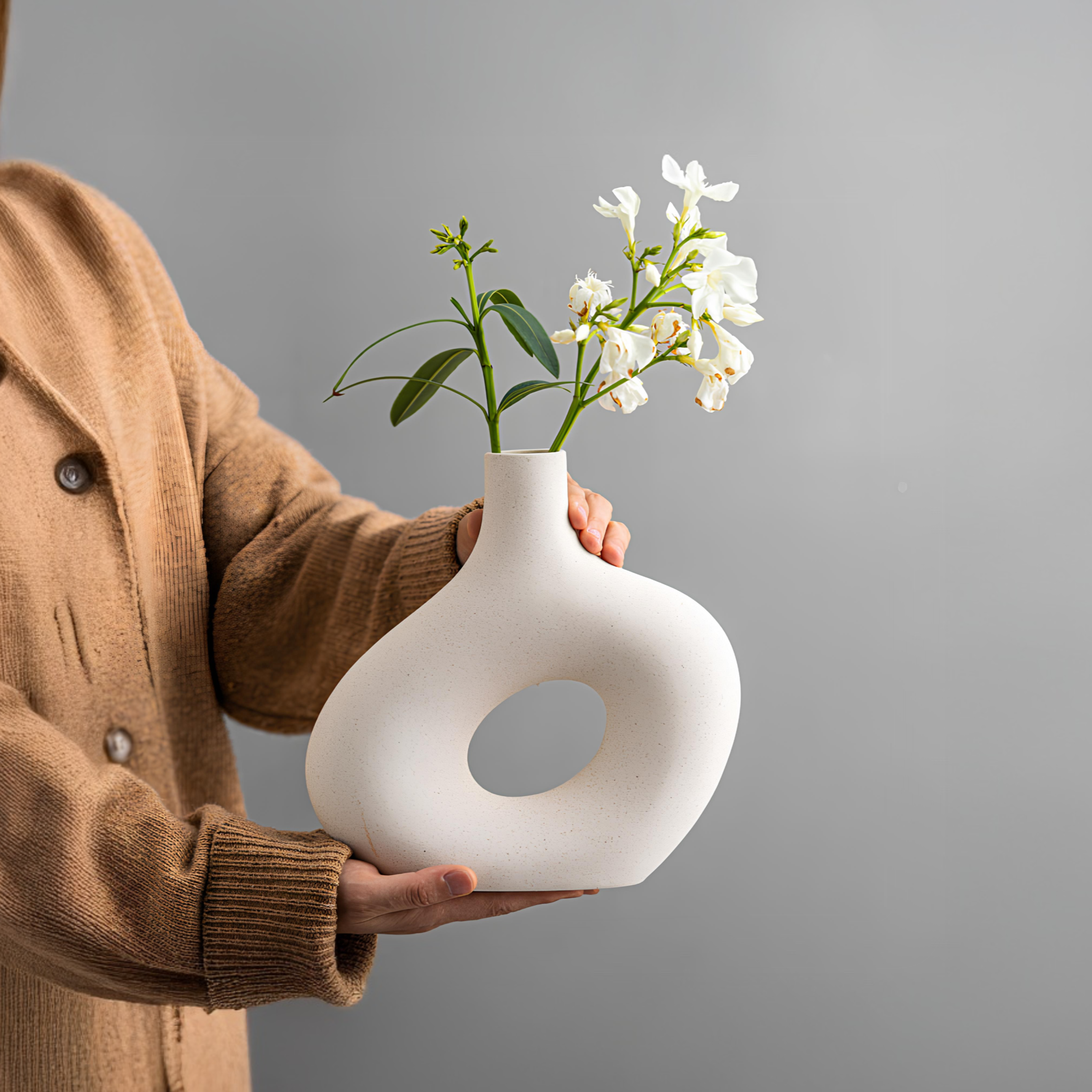 Person holding a white vase with flowers against a gray background