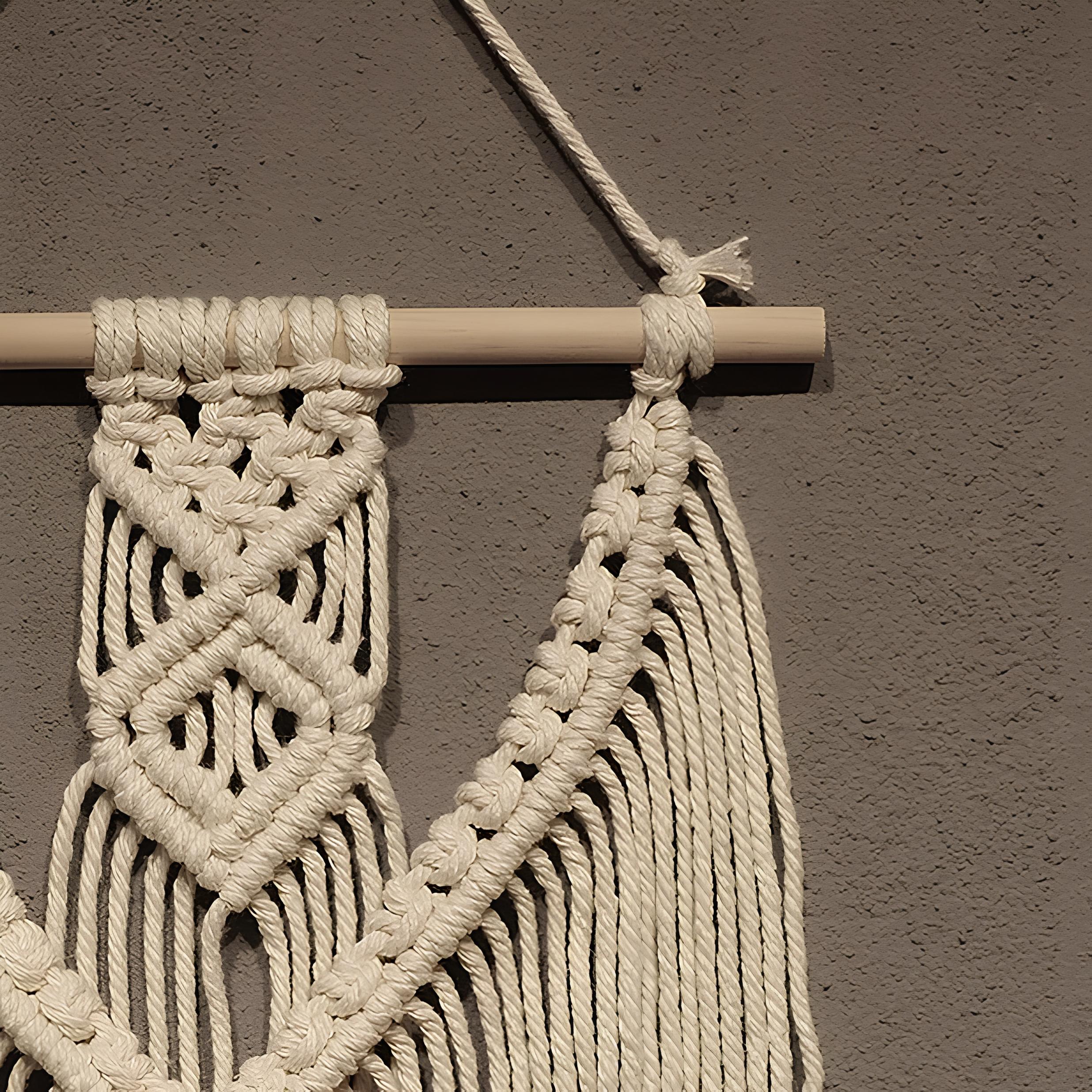 Macrame wall hanging with braided design on a wooden rod against a gray wall.