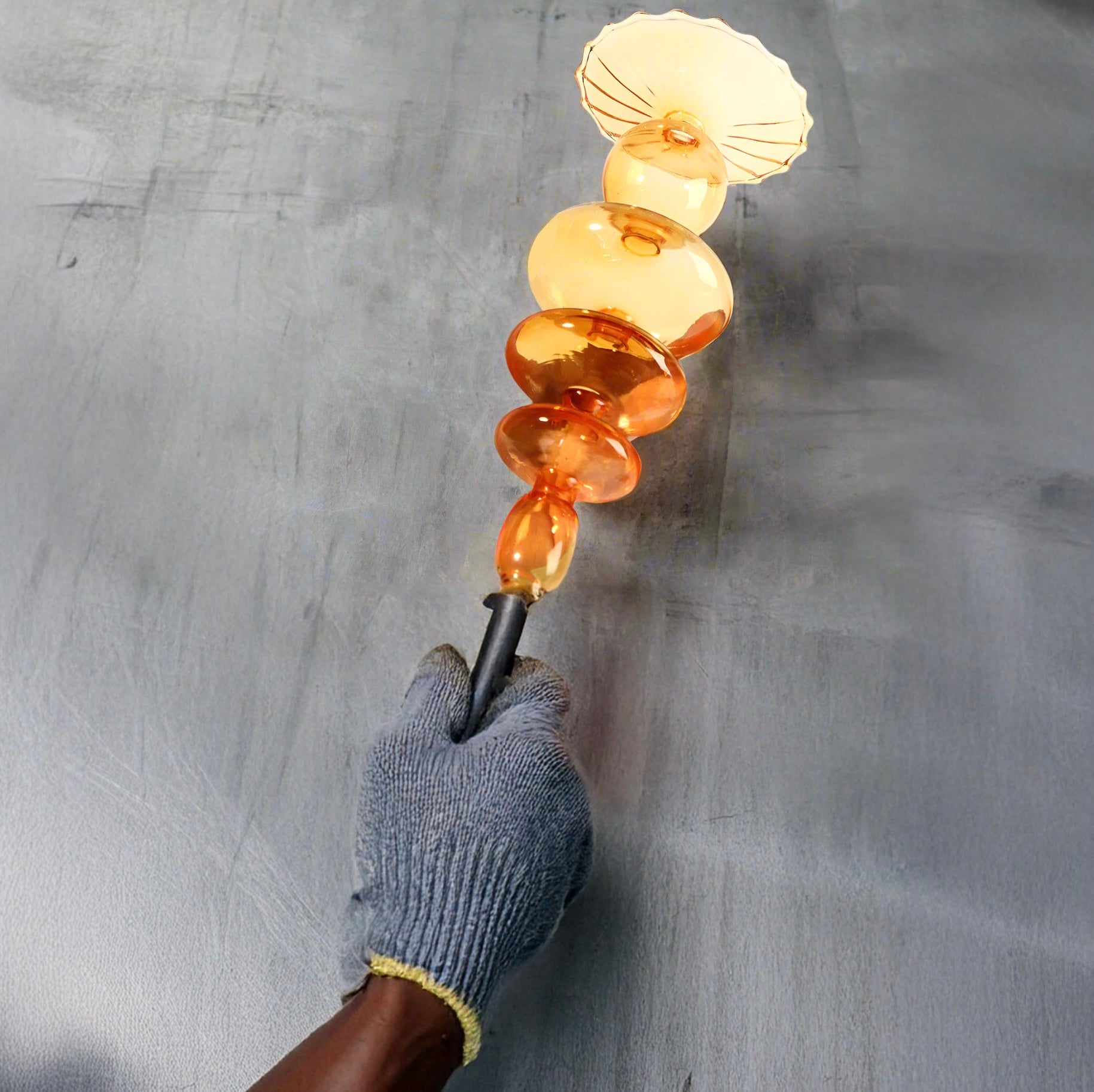 Hand holding a tool with melted glass beads against a concrete background