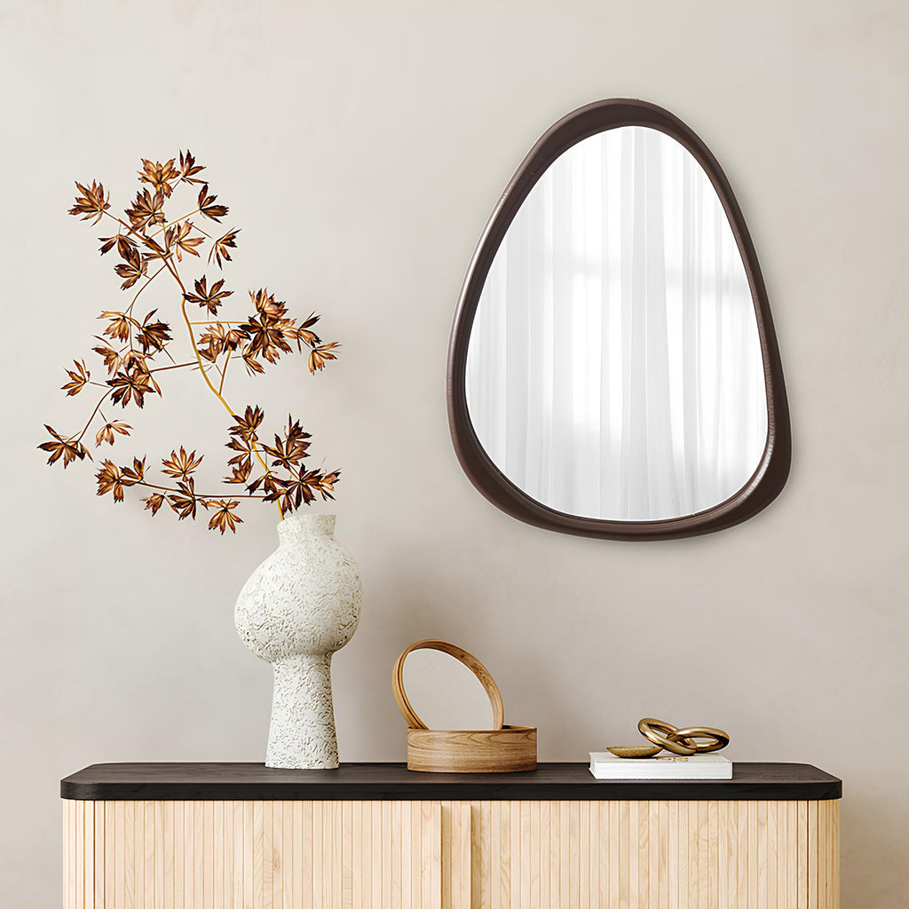 Decorative mirror with a vase and branches on a wooden console table against a beige wall.