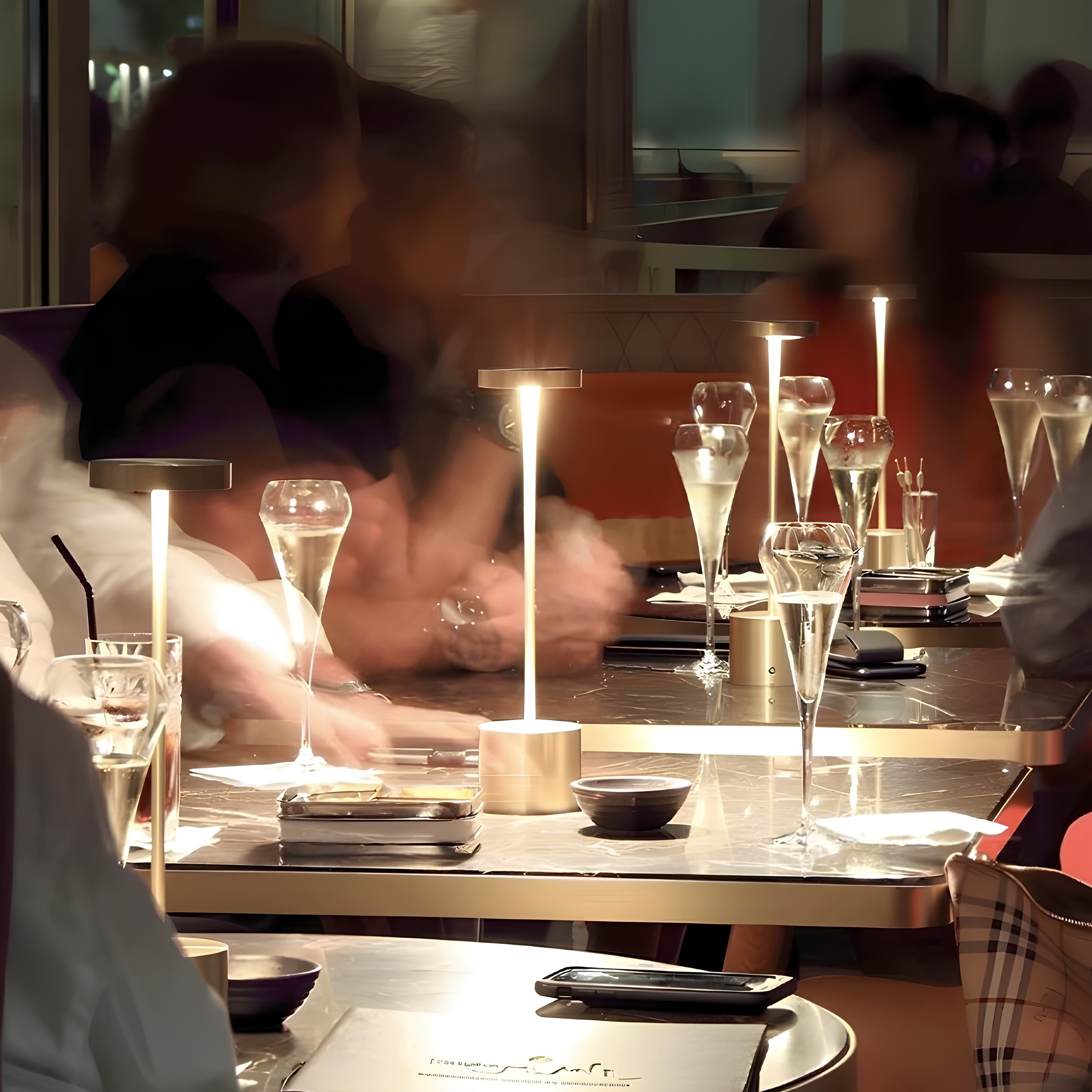 People dining at a restaurant with glasses of champagne and table lamps on a table.